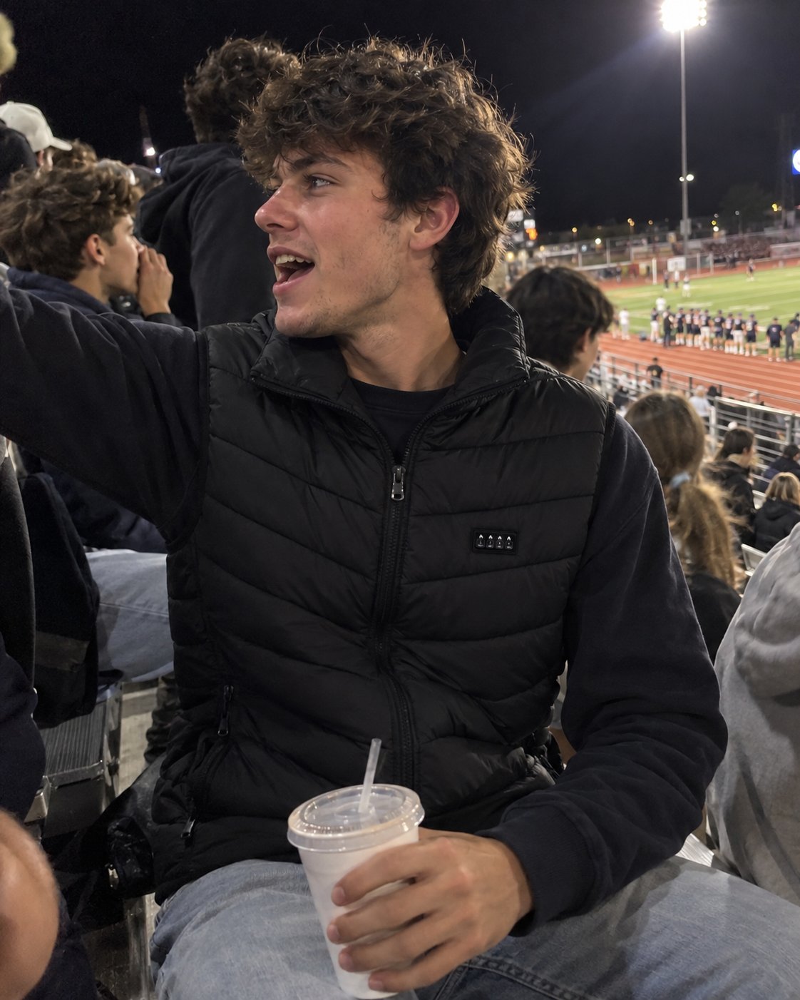 Man in the heated vest in the bleachers at a night football game